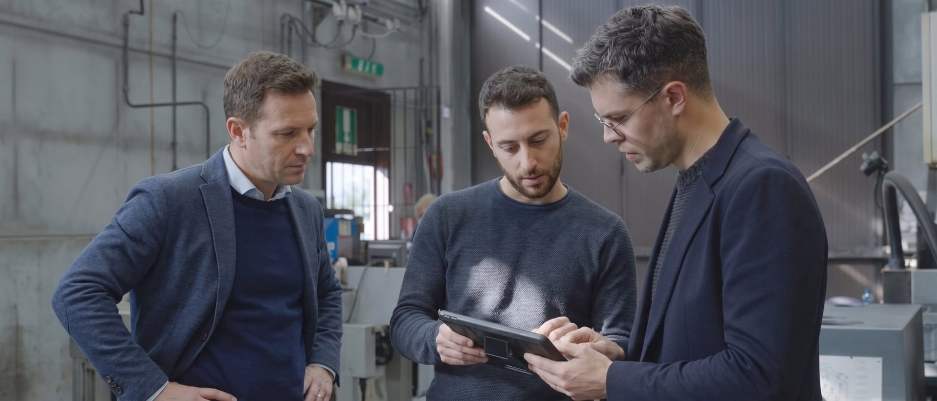 In reparto, tre persone consultano insieme un tablet accanto alle macchine